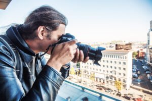 Private detective taking photo from balcony of building with professional camera